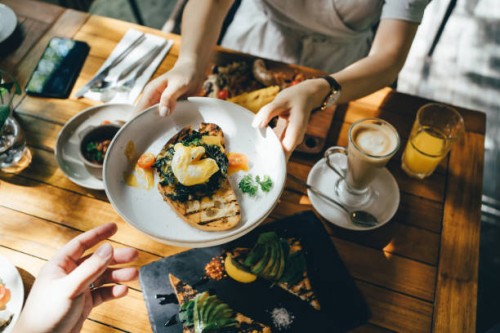 high angle view of woman passing platter of food to friend during brunch in an outdoor restaurant against beautiful sunlight - food fotografías e imágenes de stock