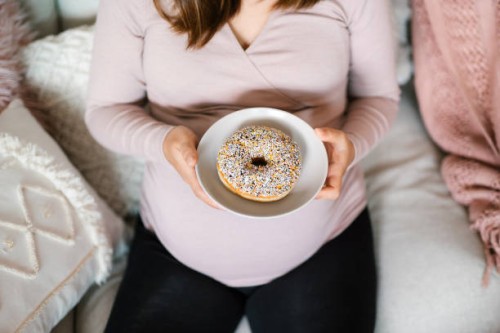 high angle view of young pregnant woman holding a plate of donut, enjoying her cravings. unhealthy diet during pregnancy. food cravings during pregnancy - junk food stock pictures, royalty-free photos & images