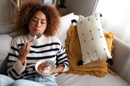 high angle view of young relaxed happy multiracial latina woman eating healthy granola and yogurt breakfast sitting on the couch at home cozy living room. copy space. - food photos et images de collection