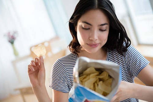 hispanic woman reading ingredients on bag of potato chips - junk food stock pictures, royalty-free photos & images