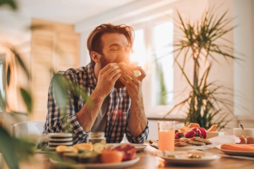 homme barbu ayant un sandwich pour le petit déjeuner à la maison. - food photos et images de collection
