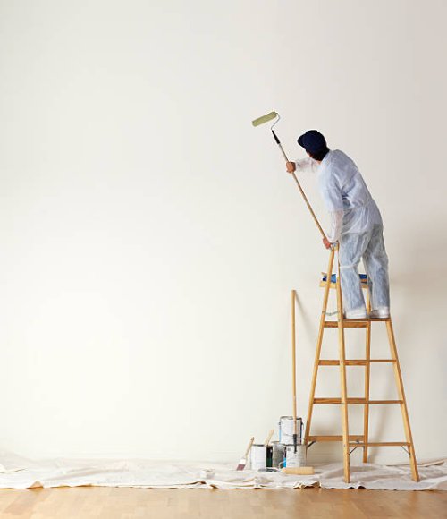 house painter standing on ladder painting a large wall - home decoration stock pictures, royalty-free photos & images