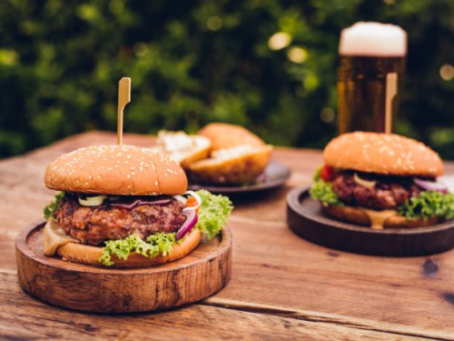 huge gourmet cheese burgers on a rustic wooden table outdoors - food stockfoto's en -beelden