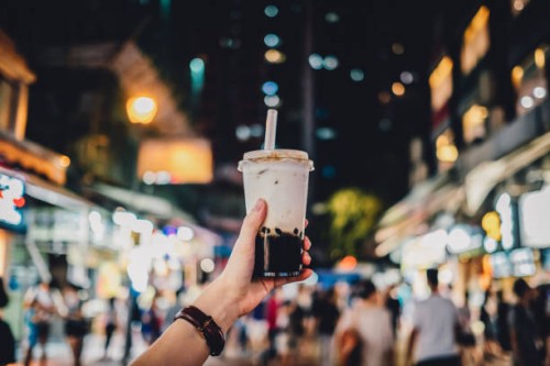 human hand holding a bottle of iced cold bubble tea against busy city street at night - junk food stock pictures, royalty-free photos & images