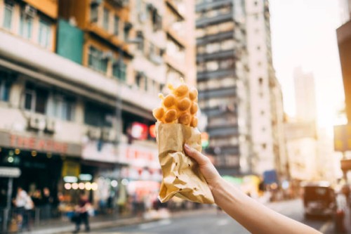human hand holding freshly made traditional street snack egg waffle against city street in hong kong - junk food stock pictures, royalty-free photos & images