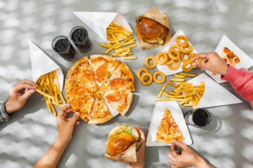 human hands with assorted take out food such as pizza, french fries, onion rings, burger and cola. - junk food stock pictures, royalty-free photos & images