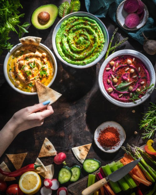 hummus bowls of chickpeas, avocado and beetroot female hand dip with cut vegetables for dipping - food stock pictures, royalty-free photos & images
