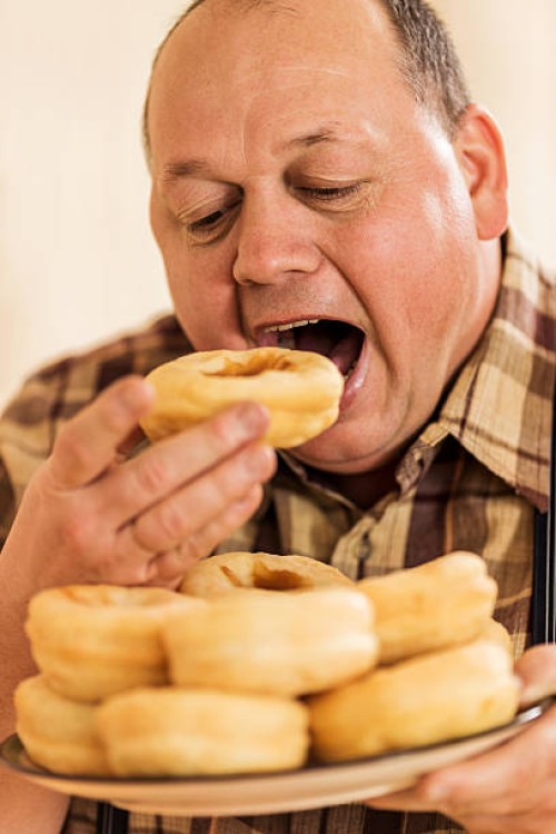 hungry overweight man eating donuts. - junk food stock pictures, royalty-free photos & images