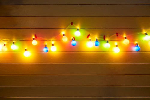 illuminated colorful string lights for party decoration at a yellow painted wooden wall in the evening - garden decoration stock pictures, royalty-free photos & images