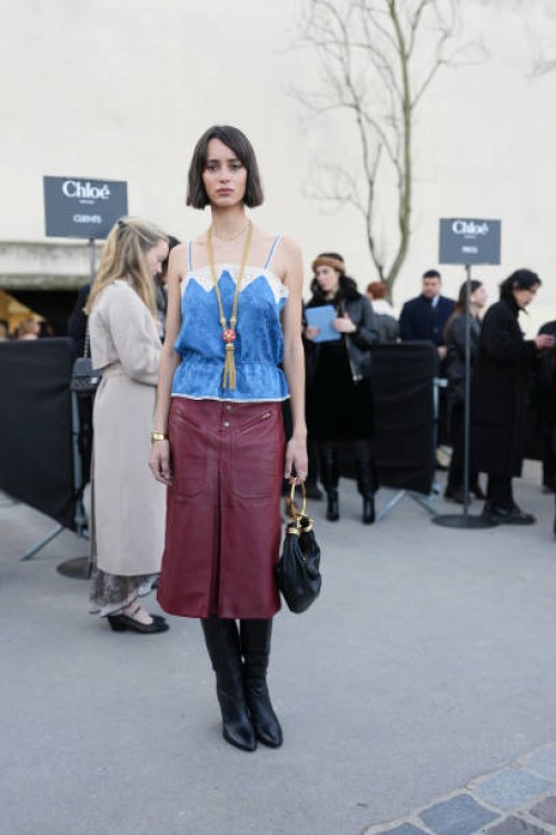 Iman Perez wears dark brown short hair, gold Chloe necklace, bright blue floral pattern lace top shiny burgundy bordeaux high slit midi leather...