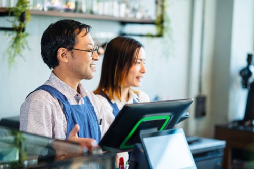 improve and increase the customer experience in coffee shops. shot of a male japanese coffee shop owner and a female waitress at a cashier counter and greeting customers as they enter the coffee shop. - junk food stock pictur