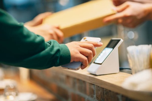 in the restaurant, a woman uses her smartphone to make a payment with the cashier. she scans the qr code using a card reader to complete a convenient contactless payment. at the same time, the cashier hands over the purchased