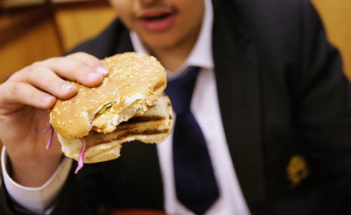 In this photo illustration a school student eats a hamburger as part of his lunch which was brought from a fast food shop near his school, on October...