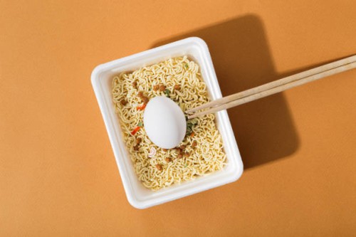 instant noodles with fresh egg in a white plastic plate, on an orange background - junk food stock pictures, royalty-free photos & images