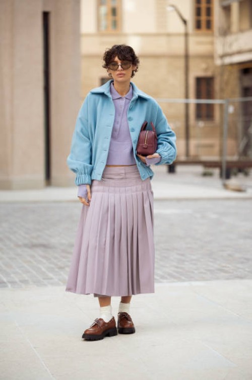 Irina Kro Eicke wears lavender midi skirt with attachable pleated part, matching top with buttons, blue jacket and brown mini bag outside the Bally...