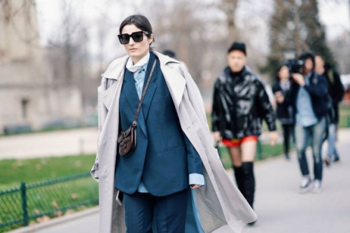 Irina Linovich wears sunglasses, a grey trench coat, a petrol-blue pantsuit, a brown alligator pattern Celine bag, outside Paco Rabanne, during Paris...