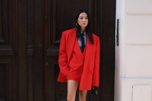 Is seen wearing a blue shirt with a black tie, a black Valentino bag, silver earrings, a red skirt, an oversized red blazer as well as a red vest...