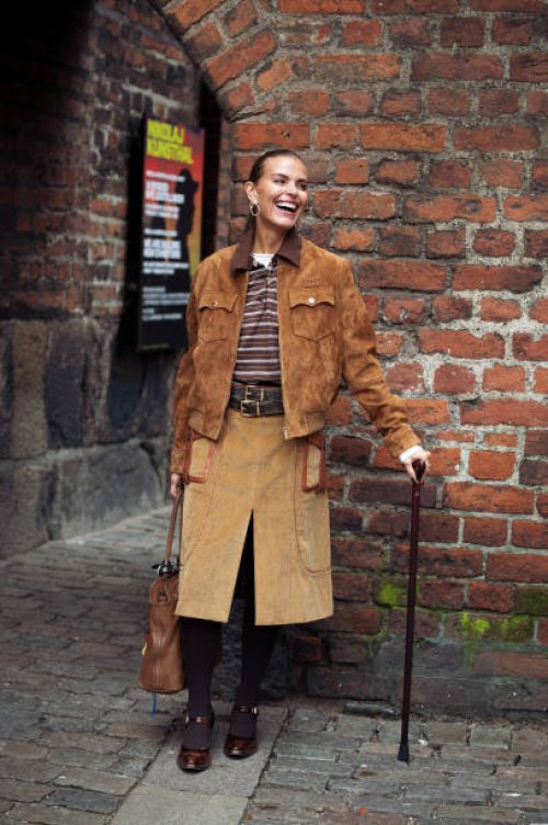 Janka Polliani wears brown cowboy shoes, brown skirt, brown suede jacket, brown striped polo shirt and a brown leather bag with bag charms or...