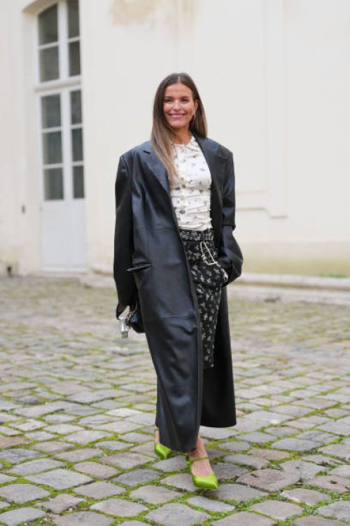 Janka Polliani wears, white floral pattern/print buttoned up Ganni shirt, shiny black leather trench coat, black belted floral pattern/print bermuda...
