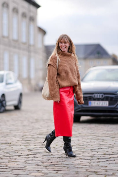 Jeanette Madsen wears a brown oversized ribbed wool pullover, a white leather bag, a red leather midi skirt, knee high high heels pointed leather...
