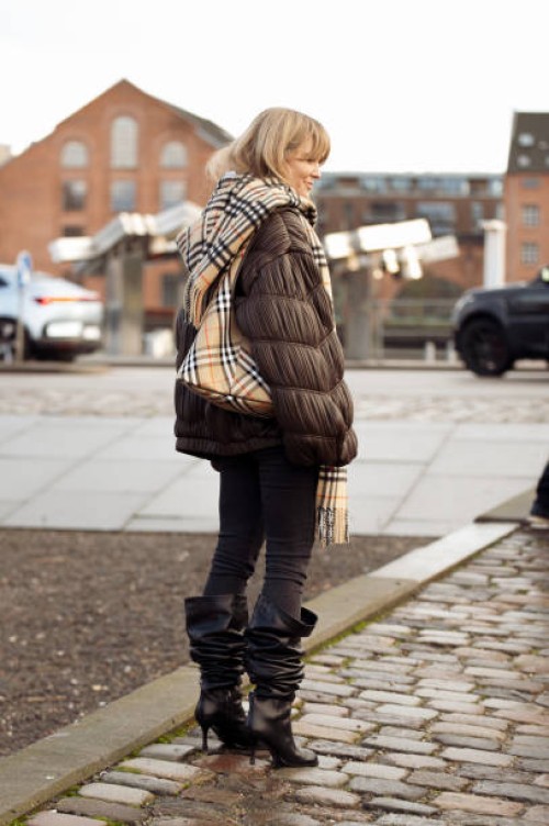 Jeanette Madsen wears black jeans, white Rotate top, brown textured leather jacket from Rotate, beige white and black checkered scarf and long...