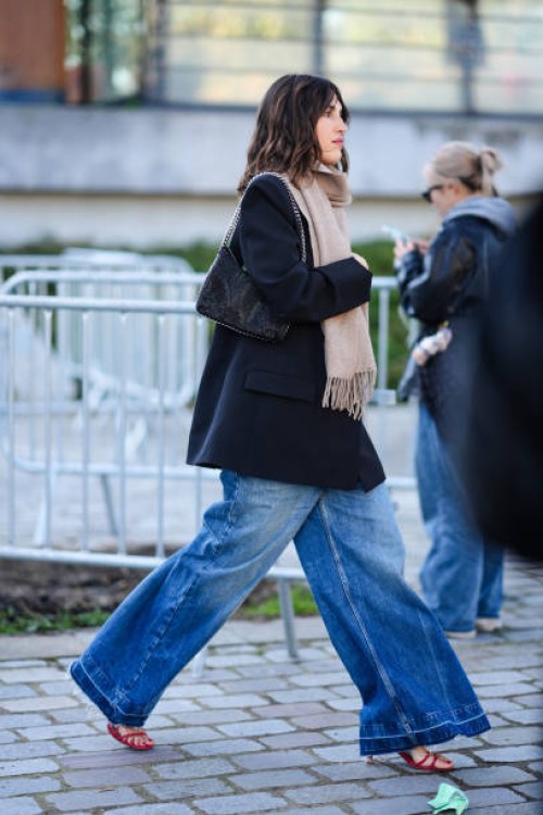 Jeanne Damas wears a beige scarf, a black bag, a black jacket, wide-leg denim jeans / pants, red high heels, outside Stella McCartney , during the...