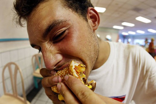 Jeff Baughman bites into his double cheeseburger with a Super Fries and a Super Coke on July 18, 2002 at a McDonalds in Miami Beach, Florida. The...