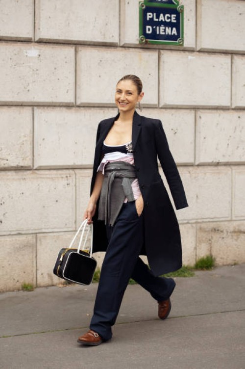 Jenny Walton wears a black and white Miu Miu leather bag, a black long coat, a grey Miu Miu sweater around the waist, a black and white Miu Miu tank...