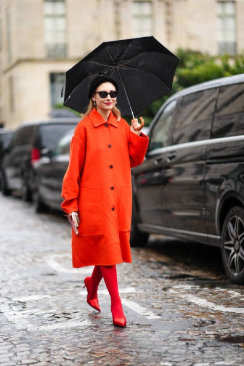 Jenny Walton wears sunglasses, a beret hat, an orange coat, red tights, high heels red shiny pointed shoes, outside Hermes, during the Womenswear...