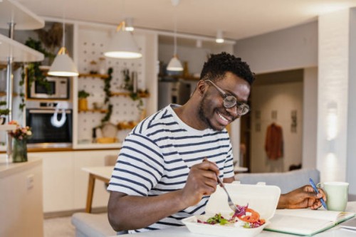 jeune homme afro-américain mangeant des repas à emporter à la maison et planifiant des activités - food photos et images de collection