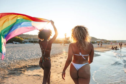 joyful friends on the beach with a rainbow flag during a parade - concert stock pictures, royalty-free photos & images