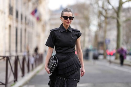 Julia Comil wears black sunglasses, a black top / jacket with ruffle details, a black leather bag with studs, outside Rokh, during the Womenswear...