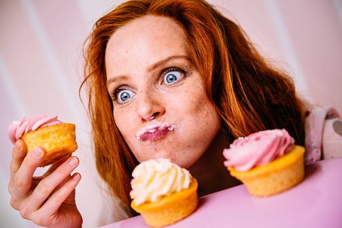 junge frau isst cupcakes mit viel enthusiasmus - food stock-fotos und bilder
