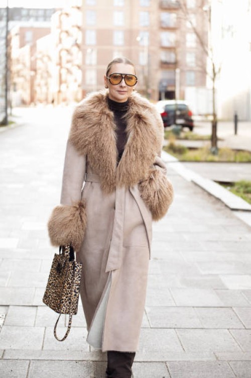 Justyna Czerniak wears long beige coat with fur, yellow sunglasses and animal print bag outside A. Roege Hove show during the Copenhagen Fashion Week...