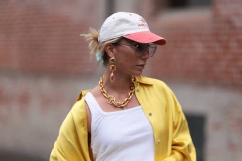 Karin Teigl seen wearing Andy Wolf light blue transparent pilot sunglasses, red / white baseball cap, gold earrings and statement chain necklace,...