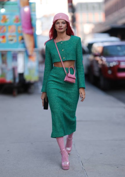 Kate Applepie is seen wearing a pink beanie from Kangol; a green tow-piece-suit, consisting of a cropped long-sleeved jacket with pink heart shaped...