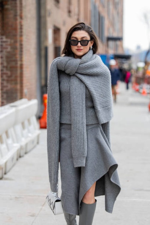 Kate Barlett wears grey knit, asymmetric skirt, boots, white bag outside Michael Kors during New York Fashion Week on February 11, 2025 in New York...