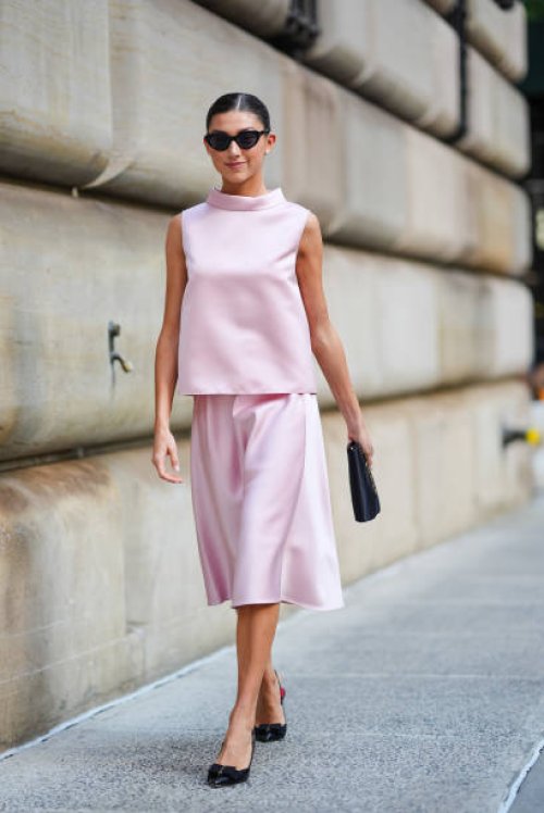 Kate Bartlett wears black sunglasses, white earrings, light pink sleeveless Carolina Herrera shirt, light pink Carolina Herrera midi skirt, black...