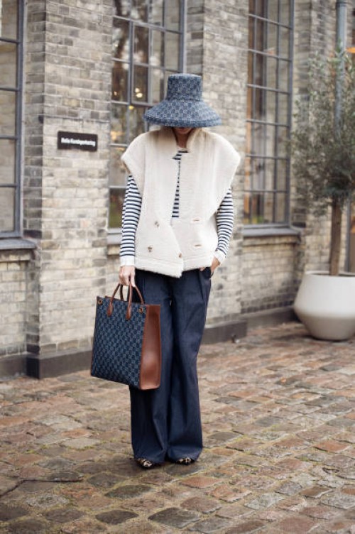 Katya Tolstova wears white and black stripped long sleeve top, white vest, blue jeans, blue hat, animal print pointy shoes, blue and brown bag...