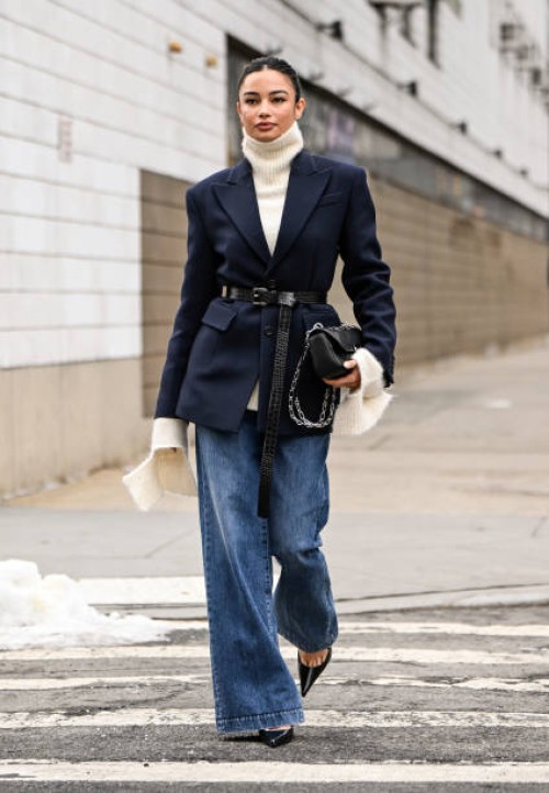 Kelsey Merritt is seen wearing a Michael Kors Collection blue jacket, cream sweater, blue jeans, black belt and Michael Kors Collection black chain...