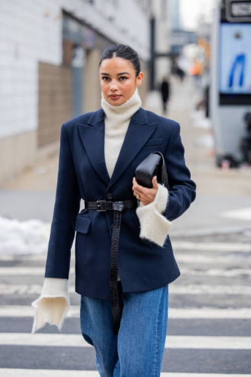 Kelsey Merritt wears navy belted blazer, denim jeans, black bag, creme white turtleneck knit outside Michael Kors during New York Fashion Week on...