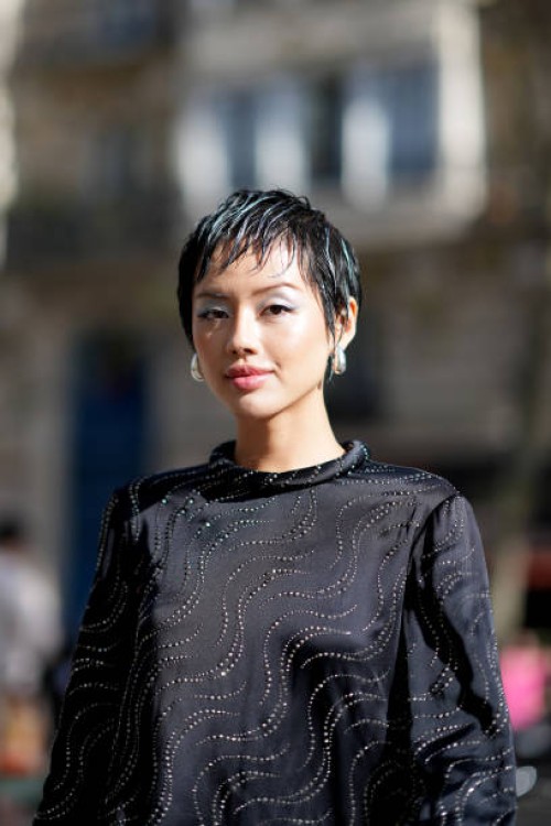 Khanh Linh wears earrings, a black lustrous silk mini dress with long sleeves and printed geometric patterns, outside Stella McCartney, during the...
