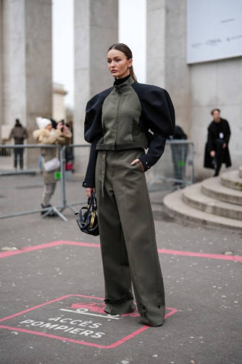 Kristina Romanova wears a khaki and black jacket, khaki wide-leg pants, a black leather bag with gold details, outside Sacai, during the Menswear...