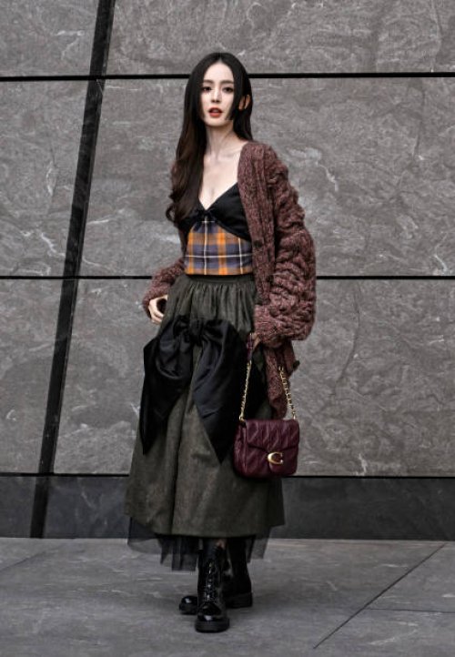 Lực Na Trát is seen wearing a brown cardigan, plaid top, brown and black ruffled skirt, black Coach boots and Coach bagoutside the Coach 1941 show...