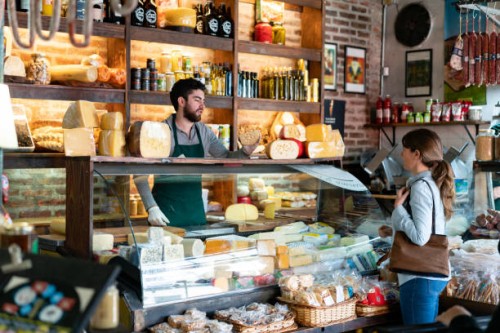 latin american man working at a delicatessen suggeting a type of cheese to female customer - food stock pictures, royalty-free photos & images