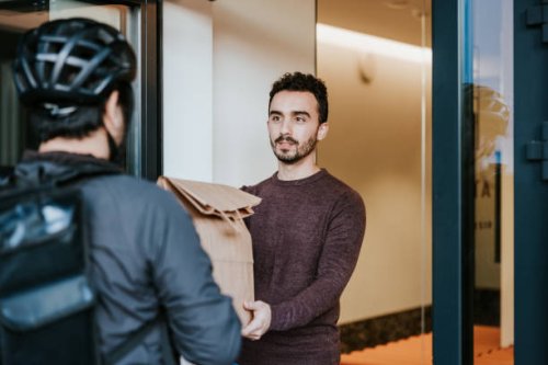 latin man receiving takeaway from a courier - food stock pictures, royalty-free photos & images
