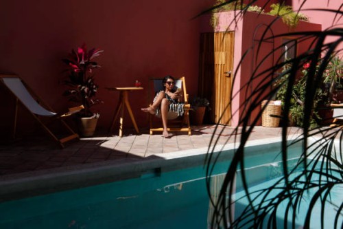 latin woman seated in a chair by swimming pool, looking at mobile phone - fashion stock pictures, royalty-free photos & images