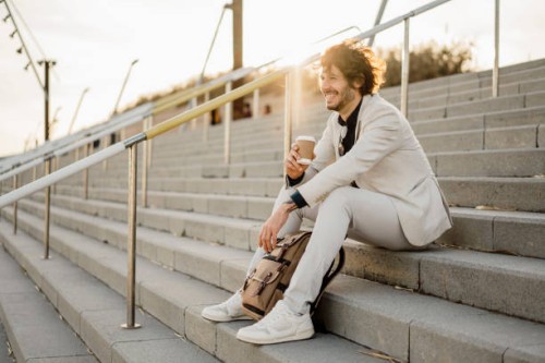 laughing businessman with coffee to go and backpack sitting on stairs outdoors - junk food stock pictures, royalty-free photos & images