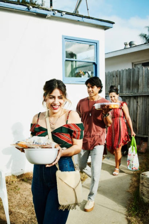 laughing friends walking into backyard with trays of food for barbecue on summer evening - food photos et images de collection