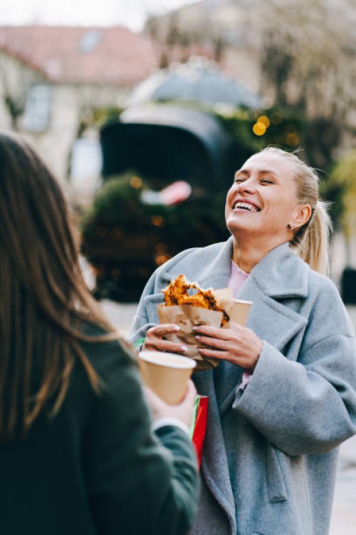 laughing women hold christmas presents and street food enjoying christmas market with friend - junk food stock pictures, royalty-free photos & images